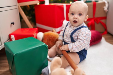 Photo for Adorable caucasian baby holding horse toy sitting on floor by christmas tree at home - Royalty Free Image