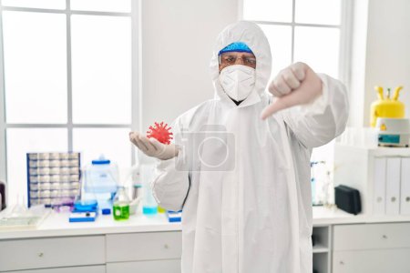 Photo for Hispanic young man working at scientist laboratory holding virus toy with angry face, negative sign showing dislike with thumbs down, rejection concept - Royalty Free Image