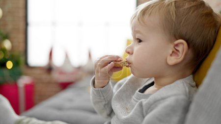 Photo for Caucasian toddler sitting on the sofa eating cookies at home - Royalty Free Image