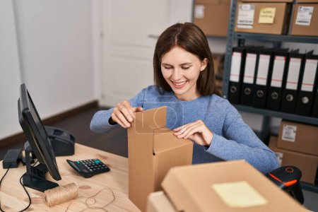 Téléchargez les photos : Jeune femme blonde ecommerce travailleur d'affaires faire boîte de carton au bureau - en image libre de droit