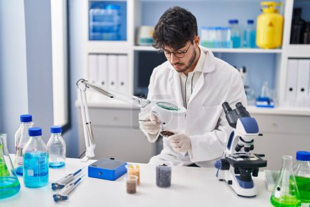 Téléchargez les photos : Young hispanic man scientist looking sample with loupe at laboratory - en image libre de droit