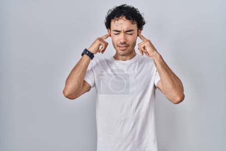 Téléchargez les photos : Homme hispanique debout sur fond isolé couvrant les oreilles avec des doigts avec une expression agacée pour le bruit de la musique forte. concept sourd. - en image libre de droit