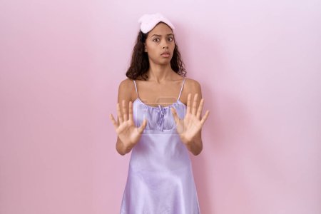 Photo for Young hispanic woman wearing sleep mask and nightgown moving away hands palms showing refusal and denial with afraid and disgusting expression. stop and forbidden. - Royalty Free Image