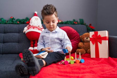 Foto de Adorable niño hispano jugando con el juguete del tren sentado en el sofá por la decoración de Navidad en casa - Imagen libre de derechos