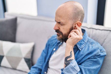 Photo for Young bald man suffering for ear pain sitting on sofa at home - Royalty Free Image