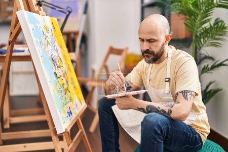 Téléchargez les photos : Jeune artiste chauve dessinant avec une expression sérieuse au studio d'art - en image libre de droit