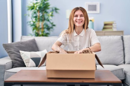Photo for Young blonde woman unpacking cardboard box at home - Royalty Free Image