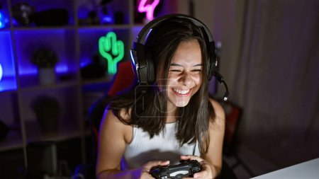 Photo for Gorgeous young hispanic woman streamer confidently owning the night. smile lit up her face, joystick in-hand, gaming away in her indoor stream room. unstoppable in the heart pumping digital universe. - Royalty Free Image