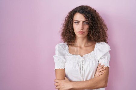 Téléchargez les photos : Hispanic woman with curly hair standing over pink background skeptic and nervous, disapproving expression on face with crossed arms. negative person. - en image libre de droit