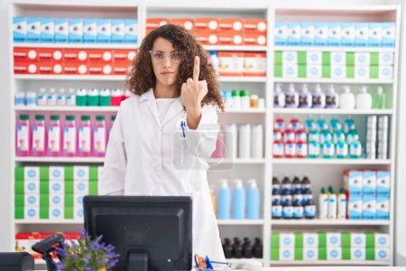 Téléchargez les photos : Hispanic woman with curly hair working at pharmacy drugstore showing middle finger, impolite and rude fuck off expression - en image libre de droit