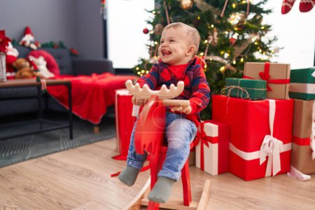 Photo for Adorable blond toddler playing with reindeer rocking by christmas tree at home - Royalty Free Image