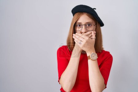 Photo for Young redhead woman standing wearing glasses and beret shocked covering mouth with hands for mistake. secret concept. - Royalty Free Image