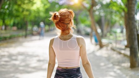 Foto de Mujer pelirroja joven usando ropa deportiva de pie hacia atrás en el parque - Imagen libre de derechos