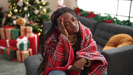Foto de Mujer africana sintiéndose enferma sentada en el sofá por el árbol de Navidad en casa - Imagen libre de derechos