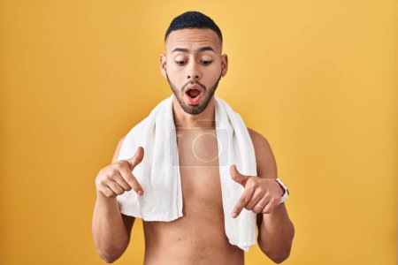 Photo for Young hispanic man standing shirtless with towel pointing down with fingers showing advertisement, surprised face and open mouth - Royalty Free Image