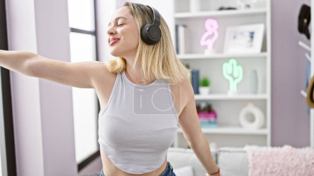 Téléchargez les photos : Young blonde woman listening to music dancing at home - en image libre de droit