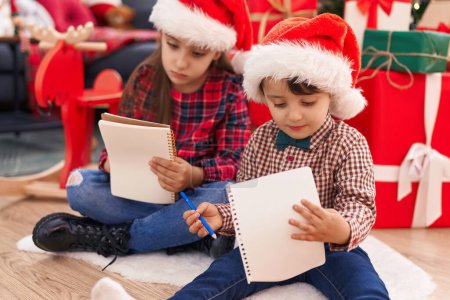 Téléchargez les photos : Adorable garçon et fille dessin sur papier célébrant Noël à la maison - en image libre de droit