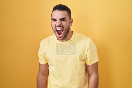Téléchargez les photos : Jeune homme hispanique debout sur fond jaune en colère et fou hurlant frustré et furieux, criant de colère. rage et concept agressif. - en image libre de droit