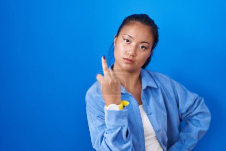 Foto de Asian young woman standing over blue background showing middle finger, impolite and rude fuck off expression - Imagen libre de derechos