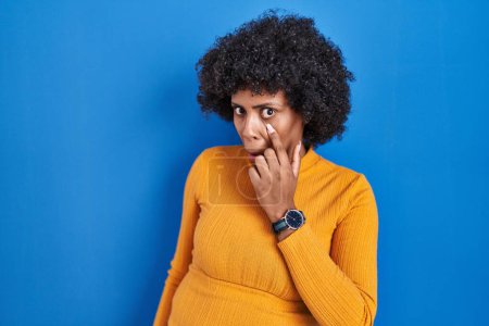 Téléchargez les photos : Femme noire avec les cheveux bouclés debout sur fond bleu pointant vers l'oeil vous regardant geste, expression suspecte - en image libre de droit