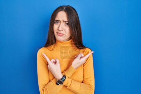 Téléchargez les photos : Jeune femme brune debout sur fond bleu pointant des deux côtés avec les doigts, direction différente en désaccord - en image libre de droit