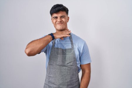 Photo for Hispanic young man wearing apron over white background cutting throat with hand as knife, threaten aggression with furious violence - Royalty Free Image