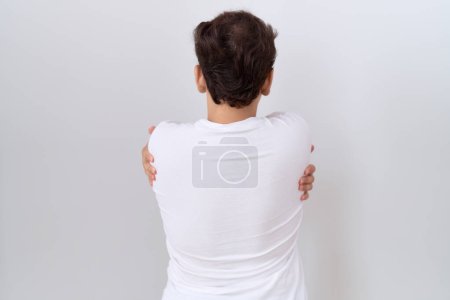 Téléchargez les photos : Jeune homme non binaire portant un t-shirt blanc décontracté s'embrassant heureux et positif à partir de l'arrière. amour de soi et soins de soi - en image libre de droit