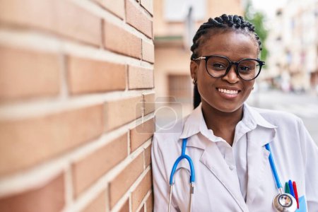 Téléchargez les photos : Femme afro-américaine médecin souriant confiant debout dans la rue - en image libre de droit