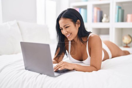 Téléchargez les photos : Jeune belle femme latine portant de la lingerie à l'aide d'un ordinateur portable dans la chambre - en image libre de droit