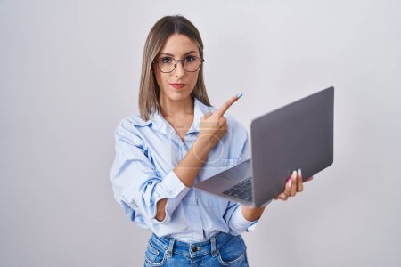 Photo for Young woman working using computer laptop pointing with hand finger to the side showing advertisement, serious and calm face - Royalty Free Image