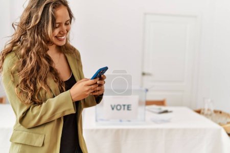 Téléchargez les photos : Young beautiful hispanic woman voter using smartphone at electoral college - en image libre de droit