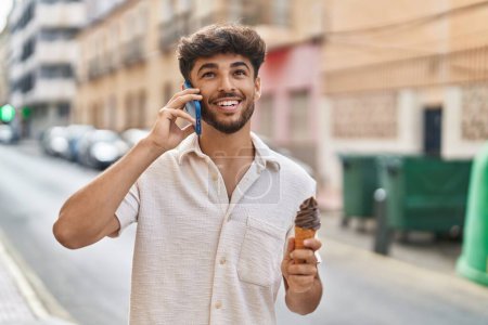 Photo for Young arab man talking on the smartphone eating ice cream at street - Royalty Free Image