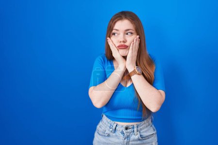 Photo for Redhead woman standing over blue background tired hands covering face, depression and sadness, upset and irritated for problem - Royalty Free Image