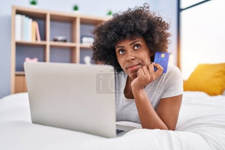 Téléchargez les photos : African american woman using laptop and credit card with doubt expression at bedroom - en image libre de droit
