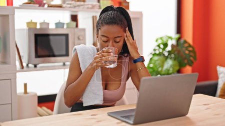 Photo for African american woman drinking glass of water using laptop at dinning room - Royalty Free Image