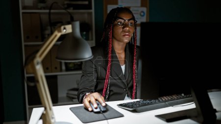 Téléchargez les photos : Patron afro-américaine ciblée gouverne son empire d'affaires jour et nuit, naviguant avec succès depuis son bureau de travail, maîtrisant Internet sur son écran d'ordinateur de bureau - en image libre de droit