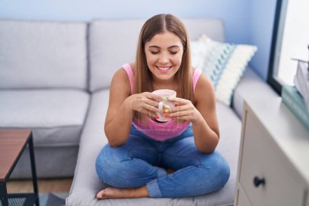 Photo for Young beautiful hispanic woman drinking coffee sitting on sofa at home - Royalty Free Image