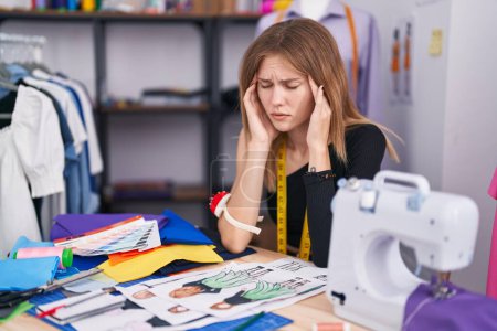 Téléchargez les photos : Jeune femme blonde tailleur assis sur la table de travail stressé au magasin de tailleur - en image libre de droit