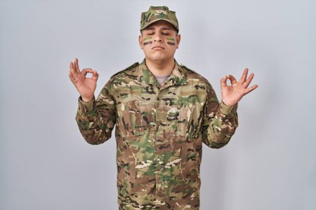 Photo for Hispanic young man wearing camouflage army uniform relax and smiling with eyes closed doing meditation gesture with fingers. yoga concept. - Royalty Free Image