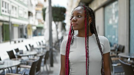 Photo for Cool african american woman with braids, seriously looking sideways on sunny coffee shop terrace, casual, urban, outdoor, relaxed female portrait living her best life in the city - Royalty Free Image