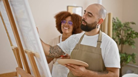 Photo for Two confident artist partners smiling together, energetically drawing in their vibrant art studio - Royalty Free Image