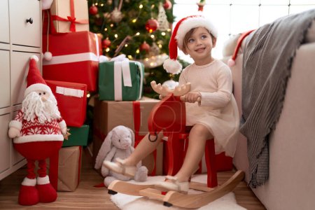 Photo for Adorable girl sitting on rocking reindeer by christmas tree at home - Royalty Free Image