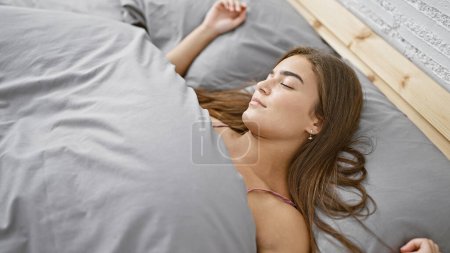 Téléchargez les photos : Détente à la maison, une jeune, belle femme hispanique se couche sur son lit douillet, confortable et parfaitement à l'aise, dérivant dans un sommeil reposant alors que la lumière du matin réchauffe sa chambre. - en image libre de droit