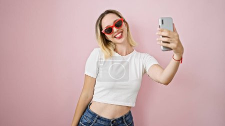 Photo for Young blonde woman wearing sunglasses make selfie by smartphone smiling over isolated pink background - Royalty Free Image