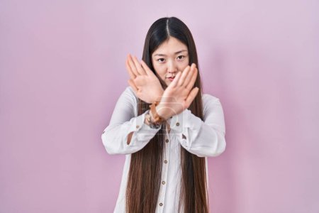 Téléchargez les photos : Jeune femme chinoise debout sur fond rose expression de rejet croisement des bras et des paumes faisant signe négatif, visage en colère - en image libre de droit