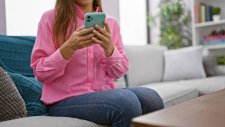 Foto de Mujer hispana hermosa joven usando teléfono inteligente sentado en el sofá en casa - Imagen libre de derechos