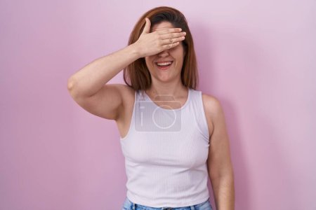 Photo for Brunette woman standing over pink background smiling and laughing with hand on face covering eyes for surprise. blind concept. - Royalty Free Image
