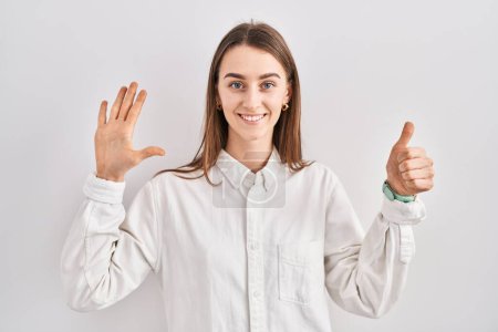 Foto de Joven mujer caucásica de pie sobre fondo aislado mostrando y señalando hacia arriba con los dedos número seis mientras sonríe confiado y feliz. - Imagen libre de derechos