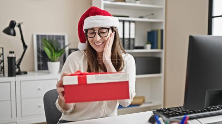 Photo for Young beautiful hispanic woman business worker holding christmas gift at office - Royalty Free Image