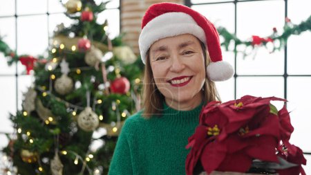 Photo for Mature hispanic woman with grey hair holding christmas plant at home - Royalty Free Image